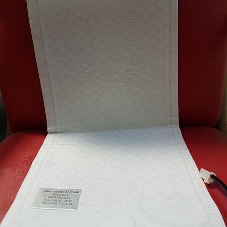 Eine weiße ausgepackte Sitzheizung fürs Auto auf einer roten Fläche platziert