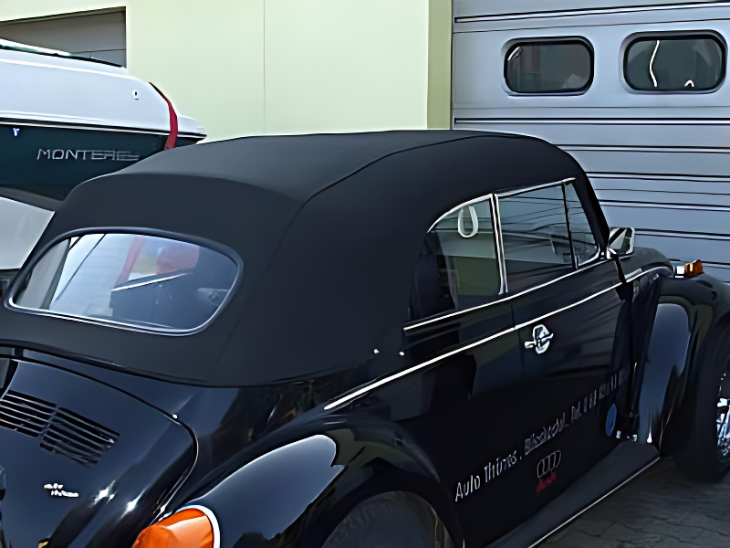 Ein schwarzer VW Käfer mit einem schwarzem Dach steht vor einem Gebäude